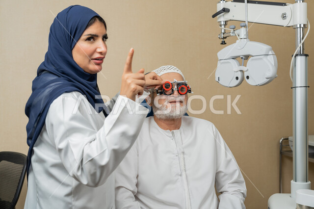 الاشارة باصبع السبابة الى مكان ما، استخدام الأجهزة الحديثة المتطورة، تشخيص وتحديد المشاكل البصرية، صورة مقربة لطبيبة عربية خليجية اماراتية تقوم بفحص عيني رجل مسن اماراتي عربي خليجي بجهاز المنظار العيني، تقييم مدى الرؤية والكشف عن الامراض العينية، مفهوم الخدمات والرعاية الصحية