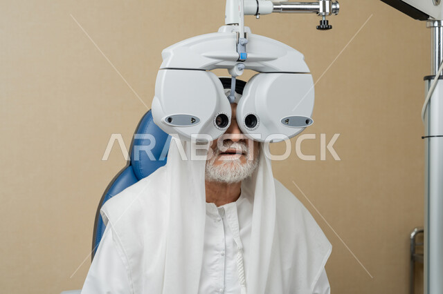 Diagnosis and identification of visual problems, close-up of an elderly Emirati Gulf Arab man wearing a ghutra in front of an optical examination device to ensure good vision, assessing vision and detecting eye diseases, the concept of services and health care in hospitals and centers, using modern advanced devices