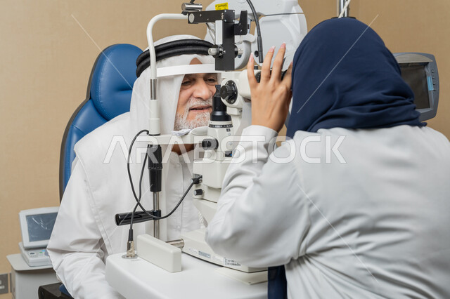 استخدام الأجهزة الحديثة المتطورة، تشخيص وتحديد المشاكل البصرية، صورة مقربة من الخلف لطبيبة عربية خليجية اماراتية تقوم بفحص عيني رجل مسن اماراتي عربي خليجي بجهاز المنظار العيني، تقييم مدى الرؤية والكشف عن الامراض العينية، مفهوم الخدمات والرعاية الصحية في المشافي والمراكز الطبية