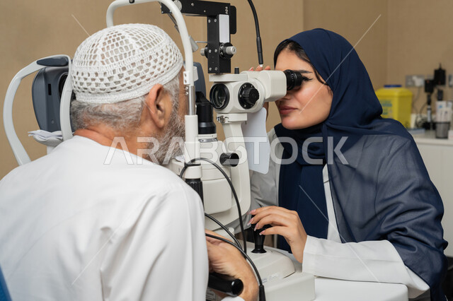 Using advanced modern devices, diagnosing and identifying visual problems, a close-up image of an Arab Gulf Emirati female doctor examining the eyes of an elderly Emirati Arab Gulf man with an ophthalmoscope, assessing vision and detecting eye diseases, the concept of services and health care in hospitals and medical centers