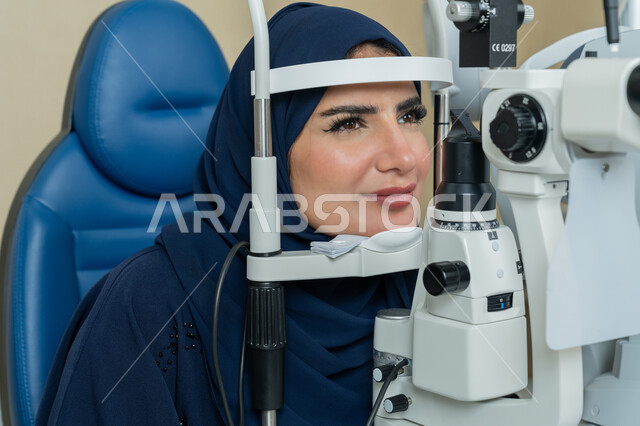 تشخيص وتحديد المشاكل البصرية، صورة مقربة لامراة عربية خليجية اماراتية ترتدي العباءة تجلس أمام جهاز فحص العين للتأكد من صحة البصر ، مفهوم الخدمات والرعاية الصحية في المستشفيات والمراكز، استخدام الأجهزة الحديثة المتطورة، الزيارة الدورية للعيادات العينية في الامارات