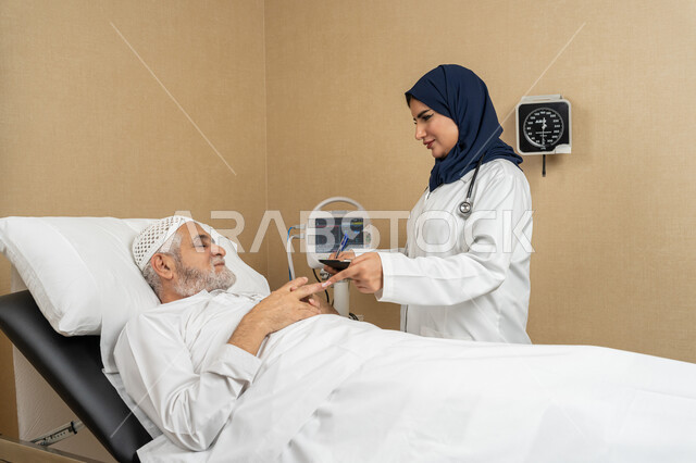 تقديم الخدمات والاستشارات الطبية للمراجعين، مفهوم الطب والرعاية الصحية، طبيبة عربية خليجية اماراتية ترتدي الحجاب والمعطف الابيض تقوم بتدوين معلومات مريض مسن عربي اماراتي مستلقي على السرير، مهن ووظائف نسائية، دراسة و مراجعة حالات المرضى