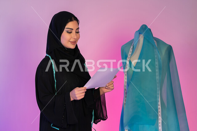 Developing technical skills, the importance of women in the field of sewing, women's professions and businesses, a close-up portrait of an Arab Gulf Emirati designer wearing an abaya and holding a dress design drawing in her hand, a young Saudi woman tailoring women's clothing, the concept of the world of fashion and style, a colorful background