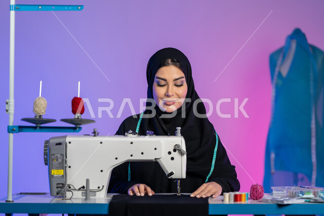 فن تصميم الأزياء, تنمية المهارات النسائية, ابتكار موديلات عصرية حديثة, تفصيل ملابس راقية, بورتريه مقرب لمصممة أزياء عربية خليجية اماراتية ترتدي العباءة تعمل على الماكينة, سيدة سعودية تجلس بإيماءات الثقة والاندماج, فنون وأعمال ومهن يدوية, خلفية ملونة