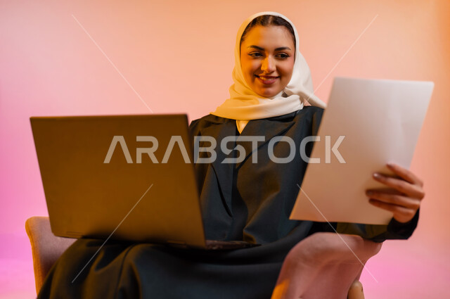 القراءة من ورقة بيضاء، بدء التدريب العملي، بورتريه لشابة عربية خليجية عمانيه محجبة ترتدي العباءة الملونة تجلس على كرسي مريح وتمسك بيدها ورقه بيضاء تقوم بقرائتها بأيماءات التركيز والاندماج، خلفيه ملونه
