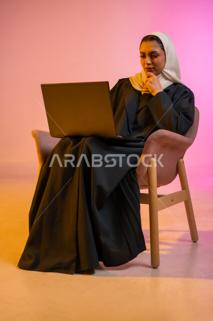 العمل لتحقيق الاهداف والاستراتيجيات، مهن ووظائف ادارية مكتبية, استخدام الأجهزة التكنولوجية الحديثة والمتطورة، إدارة شؤون الأعمال وتنظيمها، بورتريه لسيدة عربية خليجية عمانيه مبتسمه ترتدي الحجاب والعباءه تجلس عل كرسي مريح وتقوم بالعمل على جهاز الاب توب المحمول، خلفيه ملونه