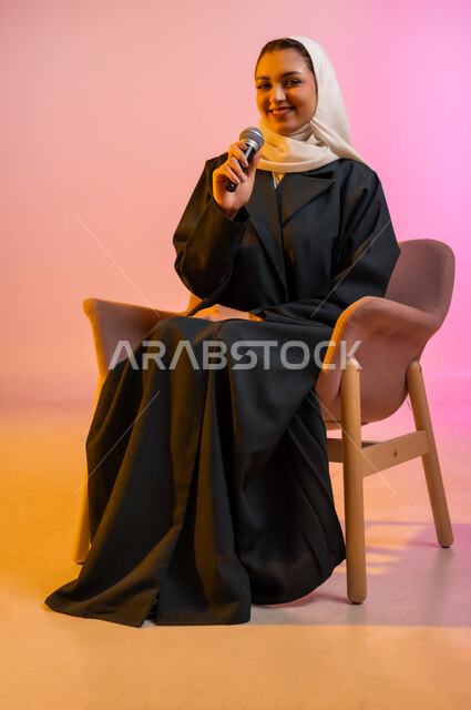 التدريب الصوتي وتقديم البرامج الاذاعيه، فن إلقاء الخطابات والندوات، بورتريه لشابة عربية خليجية عمانيه تجلس على كرسي مريح وتمسك بيدها الميكروفون، ايماءات وتعابير وجه و يدين تعبر عن الغناء والطرب، خلفية ملونه