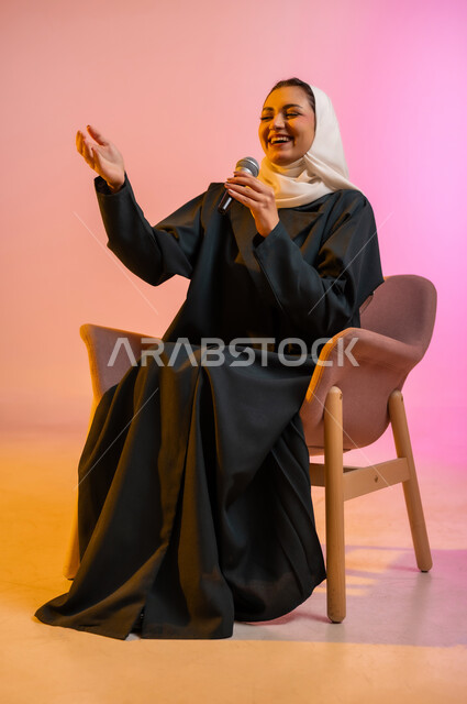 التدريب الصوتي وتقديم البرامج الاذاعيه، فن إلقاء الخطابات والندوات، بورتريه لشابة عربية خليجية عمانيه تجلس على كرسي مريح وتمسك بيدها الميكروفون، ايماءات وتعابير وجه و يدين تعبر عن الغناء والطرب، خلفية ملونه
