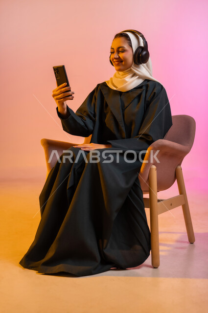 قضاء اوقات ممتعة بتبادل الاخبار والمحادثات عن بعد، بورتريه لسيده عربية خليجية عمانيه  محجبة  تقوم باجراء احاديث ودردشه مع الاهل والاصدقاء باستخدام الهاتف المحمول، ايماءات وجه تدل على السعادة و السرور، خلفيه ملونه