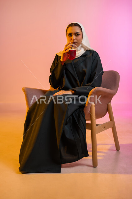 الجلسات الهادئة والاستمتاع بتناول المشروبات البارده، تناول عصائر الفواكه الطازجة، بورتريه لسيده عربية خليجية عمانيه ترتدي العباءة والحجاب تجلس على كرسي مريح تحمل بيدها كوبا من العصير الطازج وتقوم بشربه بواسطه المصاصه بايماءات السعاده والانتعاش، خلفيه ملونه
