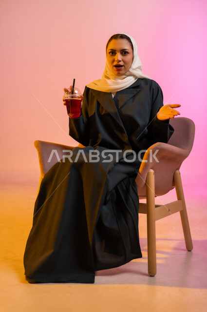 الجلسات الهادئة والاستمتاع بتناول المشروبات البارده، تناول عصائر الفواكه الطازجة، بورتريه لسيده عربية خليجية عمانيه ترتدي العباءة والحجاب تجلس على كرسي مريح تحمل بيدها كوبا من العصير الطازج وتقوم بشربه بواسطه المصاصه بايماءات السعاده والانتعاش، خلفيه ملونه