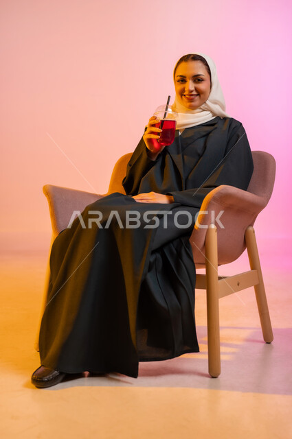 الجلسات الهادئة والاستمتاع بتناول المشروبات البارده، تناول عصائر الفواكه الطازجة، بورتريه لسيده عربية خليجية عمانيه ترتدي العباءة والحجاب تجلس على كرسي مريح تحمل بيدها كوبا من العصير الطازج وتقوم بشربه بواسطه المصاصه بايماءات السعاده والانتعاش، خلفيه ملونه
