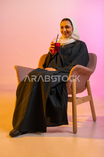 الجلسات الهادئة والاستمتاع بتناول المشروبات البارده، تناول عصائر الفواكه الطازجة، بورتريه لسيده عربية خليجية عمانيه ترتدي العباءة والحجاب تجلس على كرسي مريح تحمل بيدها كوبا من العصير الطازج وتقوم بشربه بواسطه المصاصه بايماءات السعاده والانتعاش، خلفيه ملونه