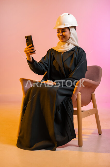 قضاء اوقات ممتعة بتبادل الاخبار والمحادثات عن بعد، بورتريه لسيده عربية خليجية عمانيه  محجبة  تقوم باجراء احاديث ودردشه مع الاهل والاصدقاء باستخدام الهاتف المحمول، ايماءات وجه تدل على السعادة و السرور، خلفيه ملونه