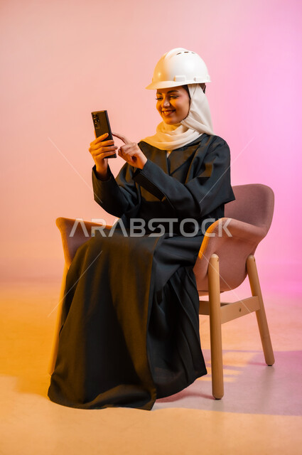 قضاء اوقات ممتعة بتبادل الاخبار والمحادثات عن بعد، بورتريه لسيده عربية خليجية عمانيه  محجبة  تقوم باجراء احاديث ودردشه مع الاهل والاصدقاء باستخدام الهاتف المحمول، ايماءات وجه تدل على السعادة و السرور، خلفيه ملونه