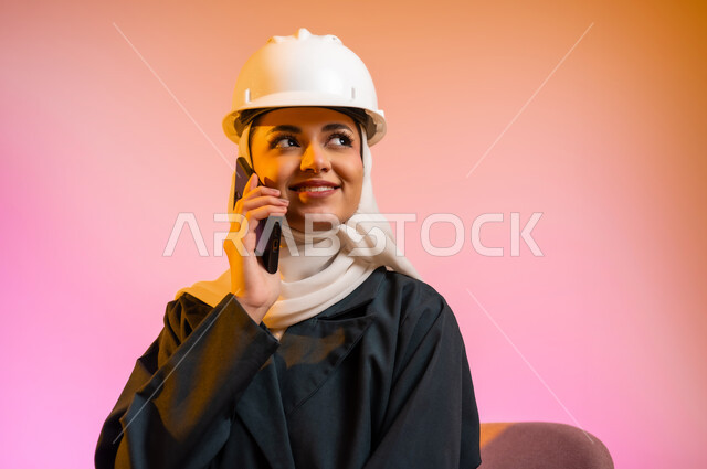 قضاء اوقات ممتعة بتبادل الاخبار والمحادثات عن بعد، بورتريه لسيده عربية خليجية عمانيه  محجبة  تقوم باجراء احاديث ودردشه مع الاهل والاصدقاء باستخدام الهاتف المحمول، ايماءات وجه تدل على السعادة و السرور، خلفيه ملونه