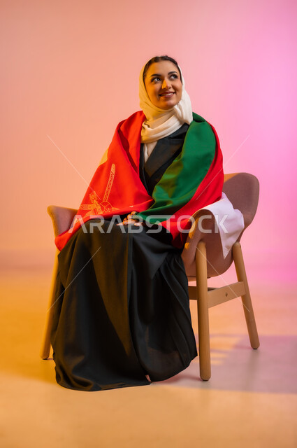 الفخر بالانتماء للهوية، المشاركة بالاعياد والمناسبات الوطنية، الاحتفال بذكرى اليوم الوطني العماني، الاعتزاز بالرموز والراية العمانية، بورتريه لشابه عربيه خليجيه عمانيه ترتدي العباءه والحجاب وتلف على جسدها العلم العماني ، مفهوم حب الوطن، خلفية ملونه