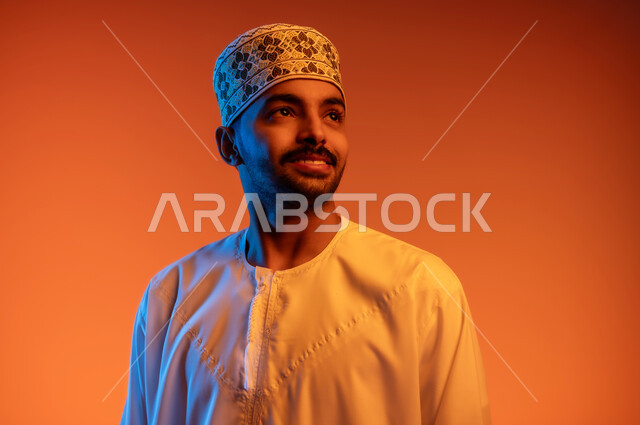 Concern for elegance and appearance, the concept of masculinity and self-confidence, taking personal photos for official documents, a portrait of a smiling young Arab Gulf Omani man wearing a dishdasha and a sleeve looking at something with gestures of pleasure and happiness, a colorful background