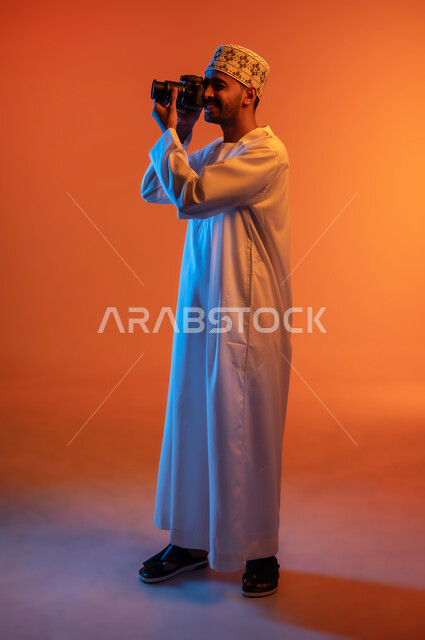 Professional photography using high-resolution digital cameras, side portrait of a professional Arab Gulf Omani photographer wearing a turban and dishdasha taking souvenir photos with a camera, Omani jobs and professions, full body length, colored background