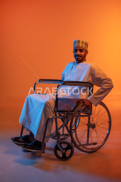 تأمين مستلزمات تساعد على الحركة والتنقل، شعور المعاقين بالإنتماء والتقدير والإحترام في سلطنة عمان، بورتريه لشاب عربي عماني خليجي مبتسم يرتدي الدشداشة و الكمه يجلس على كرسي متحرك ينظر الى الكاميرا بإيماءات السرور، خلفيه ملونة