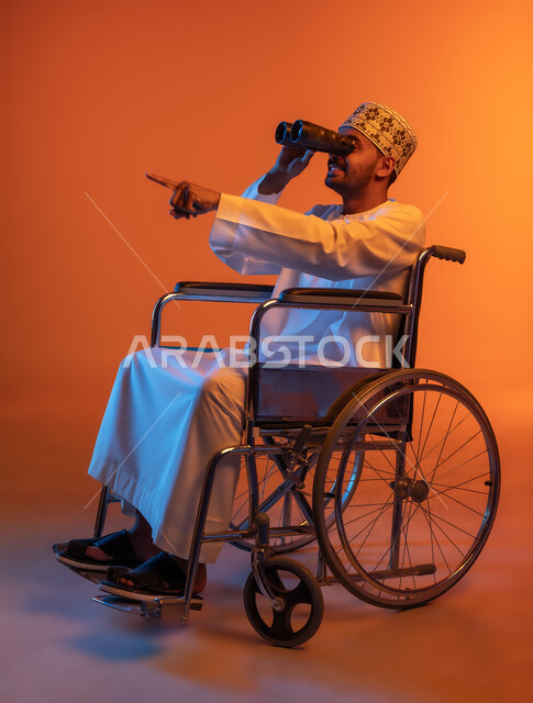 الاشارة باصبع السبابة الى شيء ما, التخطيط المستقبلي للأهداف والطموحات ،رؤية مستقبلية عند أصحاب ذوي الهمم، بورتريه من الجانب لرجل عربي خليجي عماني مقعد يرتدي الدشداشة والكمه يجلس على كرسي متحرك يحمل بيده المنظار ثنائي العينين، حب الاستكشاف والمغامرة، خلفية ملونة