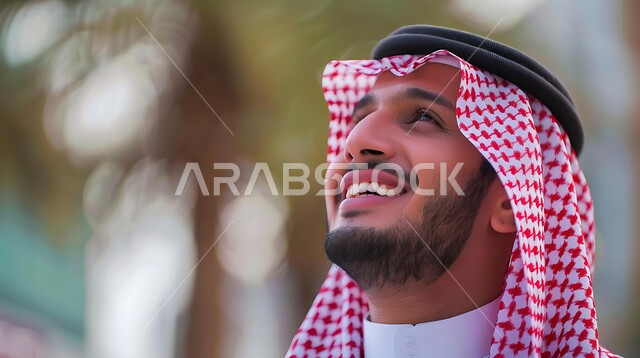 التركيز على شيء  بايماءات السرور والسعادة، مفهوم التأمل والتخطيط للمستقبل، الرجولة والأناقة والاهتمام بالمظهر الخارجي، صورة مقربة لرجل سعودي عربي خليجي مبتسم يرتدي الثوب التقليدي والشماغ ينظر إلى الأعلى بتعابير البشاشة