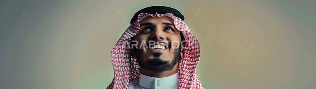 The concept of contemplation and planning for the future, manliness, elegance and interest in appearance, close-up portrait of a smiling Saudi Arabian Gulf man wearing traditional thobe and shemagh looking up with cheerful expressions, focusing on something with gestures of pleasure and happiness, background