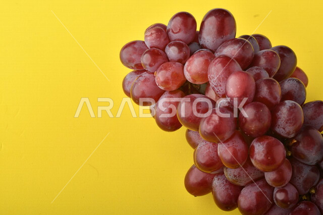 صورة لفاكهة العنب الأرجواني اللذيذ على خلفية صفراء ، فاكهة العنب الصحية اللذيذة تظهر على شكل عناقيد ، فاكهة صيفية