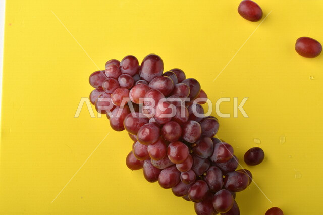 صورة لفاكهة العنب الأرجواني اللذيذ على خلفية صفراء ، فاكهة العنب الصحية اللذيذة تظهر على شكل عناقيد ، فاكهة صيفية