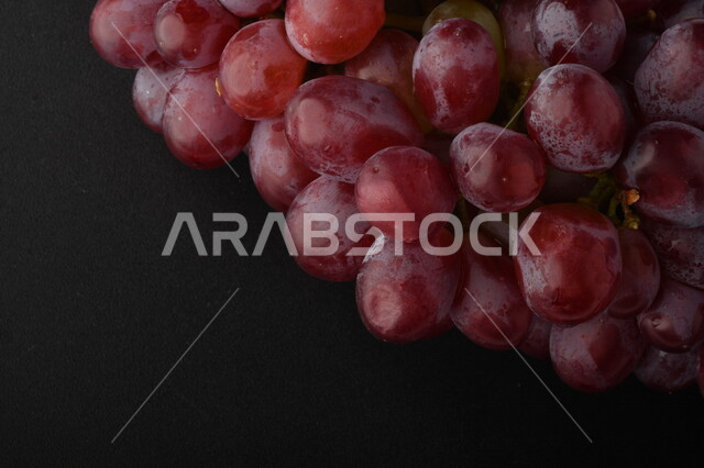 صورة لفاكهة العنب الأرجواني اللذيذ على خلفية سوداء ، فاكهة العنب الصحية اللذيذة تظهر على شكل عناقيد ، فاكهة صيفية