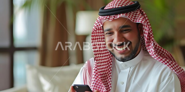 Chatting with friends via mobile programs and applications, browsing social networking sites, a Saudi Arabian Gulf man wearing a traditional shemagh and thobe holding a mobile phone in his hand, integrating modern technologies and technology into practical life, gestures of happiness and pleasure when hearing good news