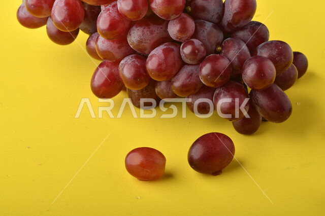صورة لفاكهة العنب الأرجواني اللذيذ على خلفية صفراء ، فاكهة العنب الصحية اللذيذة تظهر على شكل عناقيد ، فاكهة صيفية