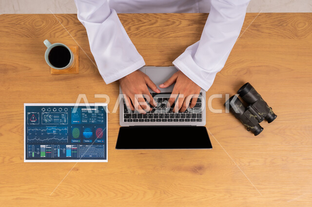 مفهوم مسح البصمات، التطور الالكتروني والنمو التكنولوجي، استخدام التقنيات الحديثة المتطورة في مجال الأمن، البحث لكشف حقائق الجرائم، عرض شاشة سوداء فارغة، صورة علوية عامودية لرجل عربي سعودي خليجي يعمل على جهاز الحاسب المحمول وبجانبه منظار وورقة المعلومات والأدلة