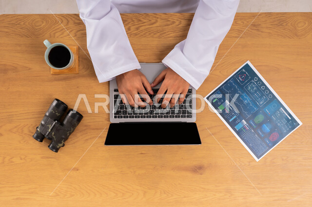 عرض شاشة سوداء فارغة، صورة علوية عامودية لرجل عربي سعودي خليجي يعمل على جهاز الحاسب المحمول وبجانبه منظار وورقة المعلومات والأدلة، مفهوم مسح البصمات، التطور الالكتروني والنمو التكنولوجي، استخدام التقنيات الحديثة المتطورة في مجال الأمن، البحث لكشف حقائق الجرائم