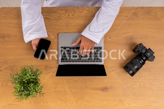 تعلم أخذ لقطات تذكارية فنية، ممارسة الهواية المفضلة بشغف، عرض شاشة سوداء فارغة، صورة علوية عامودية ليد رجل عربي سعودي خليجي يعمل على جهاز الهاتف المحمول ويجانبه كاميرا فوتوغرافية، استخدام التقنيات الحديثة المتطورة، إتقان واحتراف مهنة التصوير