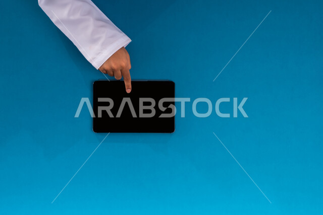 عرض شاشة سوداء فارغة، إنجاز المهام المطلوبة عن بعد، بورتريه علوي عامودي ليدين رجل عربي خليجي سعودي يعمل على جهاز الهاتف التابليت، استخدام التقنيات الحديثة والمتطورة بالعمل، البيع والشراء عبر الانترنت، الاستفادة من تطبيقات التسوق أونلاين، خلفية زرقاء