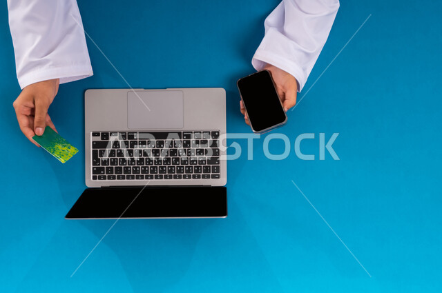 إمكانية تسديد الفواتير بالبطاقة الالكترونية، عرض شاشة سوداء فارغة، إدخال المعلومات البنكية على الحاسوب المحمول، الشراء والدفع عن بعد، بورتريه علوي عامودي ليدين رجل عربي سعودي خليجي  يقوم باستخدام بطاقة الإئتمان، التسوق الالكتروني عبر جهاز اللابتوب، خلفية زرقاء