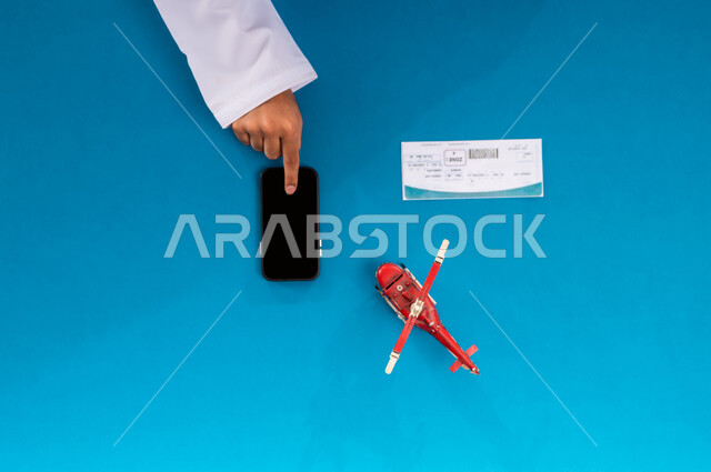 الاستعداد لقضاء رحلة صيفية ممتعة، عرض شاشة سوداء فارغة، بورتريه علوي عامودي ليد رجل عربي خليجي سعودي يستخدم جهاز الجوال وبجانبه مجسم طائرة، قطع تذاكر الطيران أونلاين، استخدام الانترنت للبحث عن رحلات جوية، مفهوم السياحة والقيام بالجولات الترفيهية، خلفية زرقاء