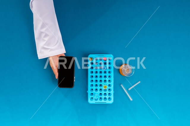 عرض شاشة سوداء فارغة، بورتريه علوي عامودي ليد رجل عربي سعودي خليجي يمسك جهاز الجوال وبجانبه أنابيب الاختبار، تدوين نتائج التحاليل المخبرية على الهاتف المحمول، إجراء تجارب وبحوث علمية عبر التكنولوجيا الحيوية، البحث والتطوير العلمي في مجال الكيمياء، خلفية زرقاء