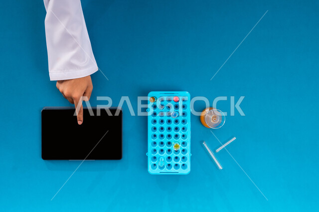 إجراء تجارب وبحوث علمية عبر التكنولوجيا الحيوية، البحث والتطوير العلمي في مجال الكيمياء، عرض شاشة سوداء فارغة، بورتريه علوي عامودي ليد رجل عربي سعودي خليجي يعمل على جهاز الآيباد وبجانبه أنابيب الاختبار، تدوين نتائج التحاليل المخبرية على التابليت، خلفية زرقاء