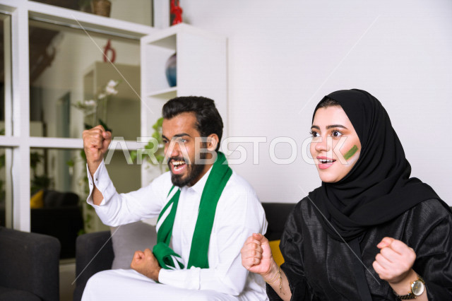 زوجان عربيان سعوديان خليجيان يشاهدان مباراة للدوري السعودي ، يشجعان فريق الأهلي و السعودية , ايماءات وجه تدل على الحماس والفرحة بالفوز , أندية وتشجيع .