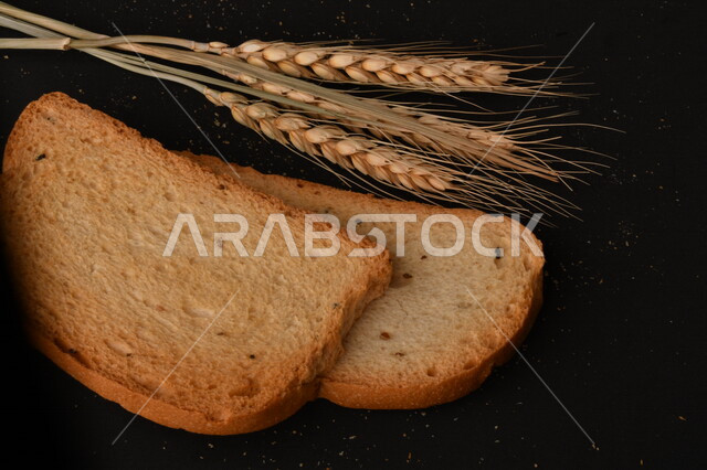 صورة مقربة لمجموعة من نباتات القمح ، وشرائح خبز التوست المحمصة على خلفية سوداء