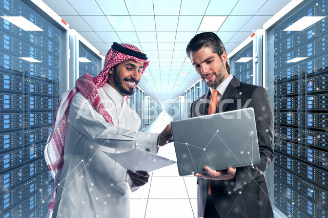 نموظف عربي سعودي خليجي يعمل في مركز البيانات يقوم باستخدام جهاز تقني لادارة الخوادم, مجموعه من خوادم الانترنت والسيرفرات , حظيرة الخوادم, تقنيه وتكنولوجيا , نقاش رجل عربي سعودي خليجي مع موظف اجنبي في غرفة مركز البيانات