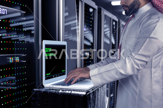 موظف عربي سعودي خليجي يعمل في مركز البيانات يقوم باستخدام جهاز تقني لادارة الخوادم, مجموعه من خوادم الانترنت والسيرفرات , حظيرة الخوادم, تقنيه وتكنولوجيا