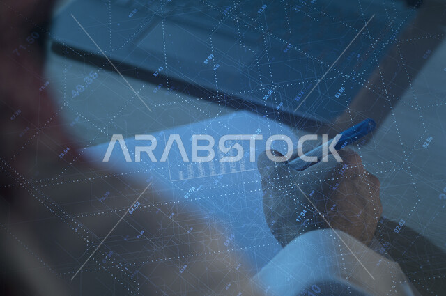 A close-up image of the hand of a Saudi Arabian Gulf man at his workplace in the company, holding his pen and solving mathematical financial matters, writing plans and data, using 3D hologram technology
