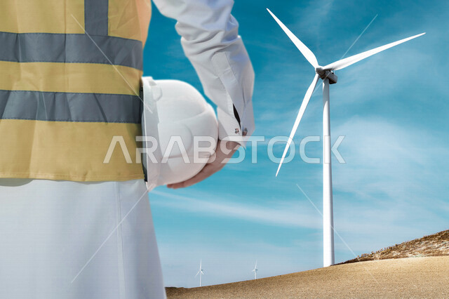 صورة من الخلف لمهندس كهربائي عربي خليجي سعودي  ، يقف أمام حقل لتوربينات الرياح و طواحين الهواء ، مفهوم استخدام الطاقة المتجددة ، مفهوم التكنولوجيا التنمية المستدامة بالطاقة البديلة