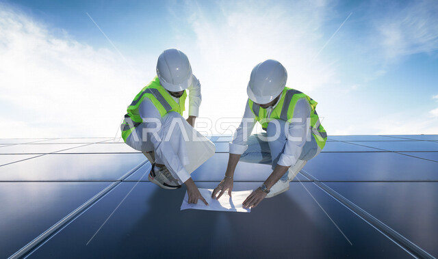 مهندسان كهربائيان عربيان خليجيان سعوديان يناقشان مخطط  لتركيب الخلايا الشمسية على لوحة الخلايا ، تقرير موجز ، استخدام الطاقة الشمسية لتوليد الكهرباء ، مفهوم استخدام الطاقة المتجددة ، مفهوم التكنولوجيا التنمية المستدامة بالطاقة البديلة