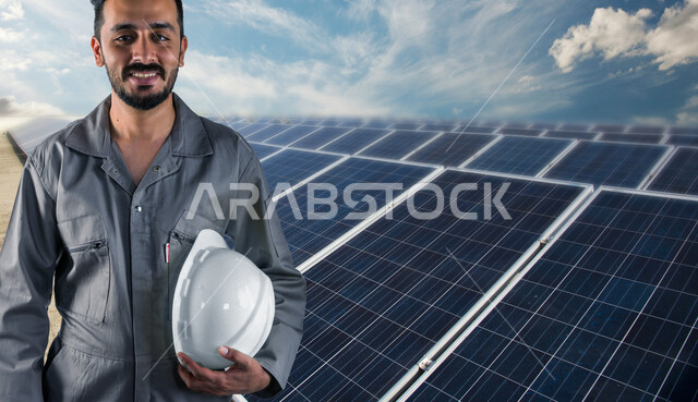 صورة لمهندس كهربائي عربي خليجي سعودي مبتسم يقف أمام لوحات للخلايا الشمسية لتوليد الكهرباء ، ايماءات وتعابير تدل على السعادة ، مفهوم استخدام الطاقة المتجددة ، مفهوم التكنولوجيا التنمية المستدامة بالطاقة البديلة