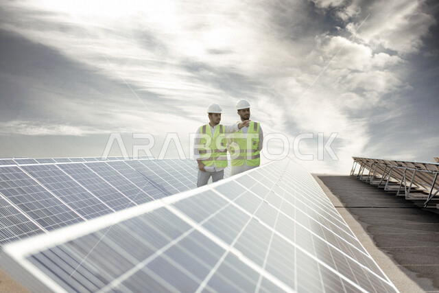 مهندسان كهربائيان عربيان خليجيان سعوديان يتفقدان تركيب الخلايا الشمسية على السطح ، استخدام الطاقة الشمسية لتوليد الكهرباء ، مفهوم استخدام الطاقة المتجددة ، مفهوم التنمية المستدامة بالطاقة البديلة