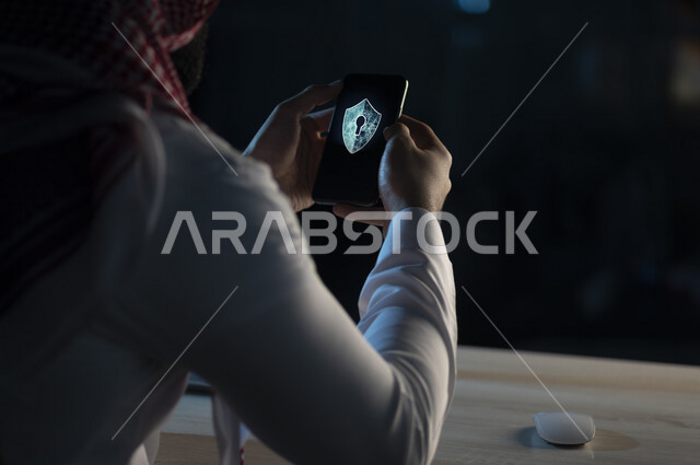 رجل عربي سعودي خليجي يمسك بيده الهاتف المحمول يحتوي على شعار القفل الالكتروني الذكي, برنامج القفل الذكي, الامن السيبراني, ادارة المخاطر وأمن المعلومات.